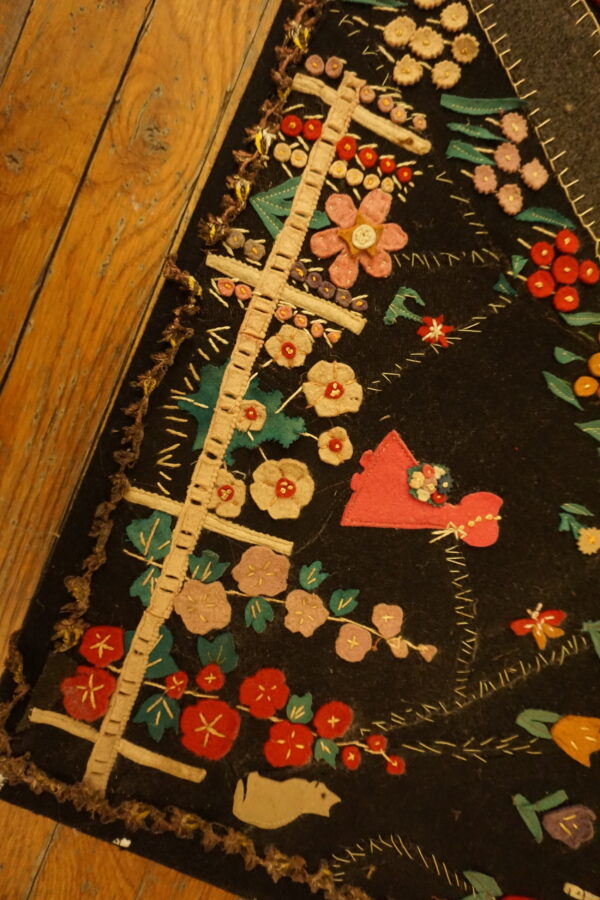 Black textile featuring colorful red, pink, and green floral and figurative appliqué on wide wooden planks.