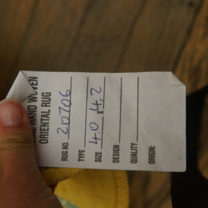 A white rug tag with size 4.0 x 4.2 is held above dark brown wood planks.