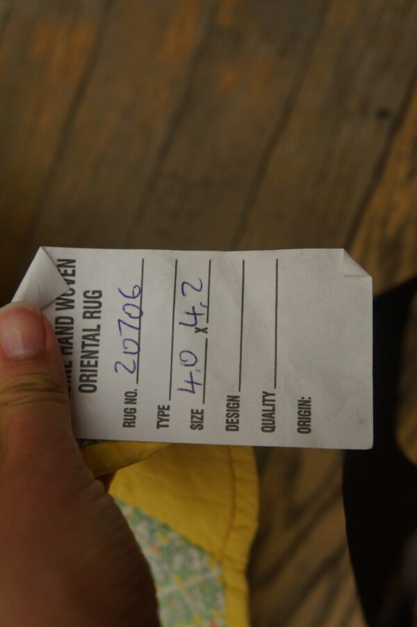 A white rug tag with size 4. 0 x 4. 2 is held above dark brown wood planks.