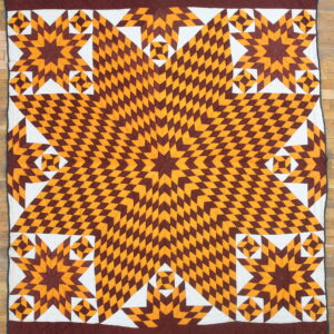 Quilted textile with a central starburst pattern in maroon and gold diamonds over hardwood.