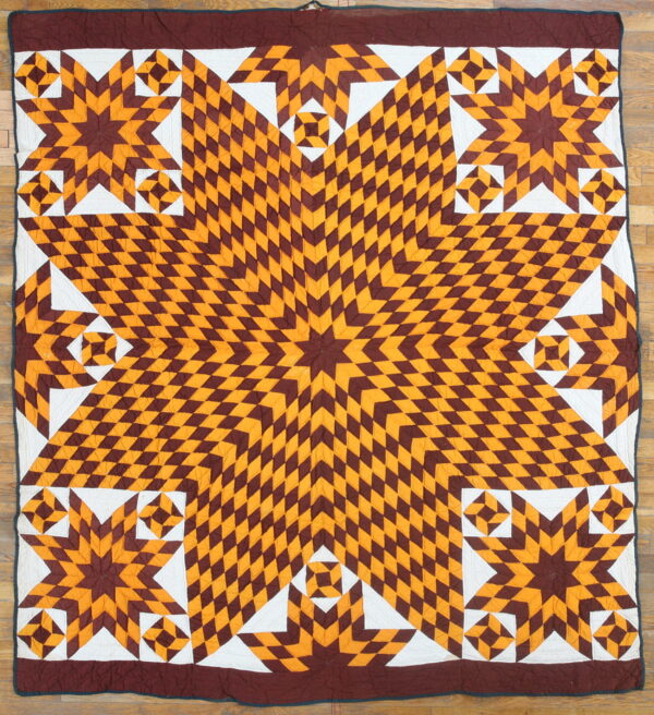 Quilted textile with a central starburst pattern in maroon and gold diamonds over hardwood.