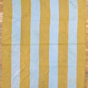 Quilted rug with wide vertical gold and pale blue stripes lies flat on a light wood floor.