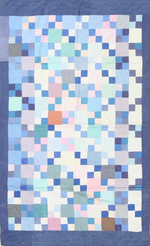 A flatweave rug with a patchwork pattern of blue, pink, lavender, and white squares, framed by a dark blue border.