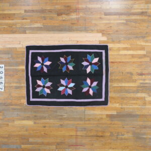 Overhead view of a black rug with multicolored stars and lavender borders, displayed on light wooden floorboards.