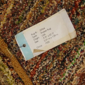 Close-up of variegated brown, red, and cream high-pile rug texture with a large white product information tag attached.