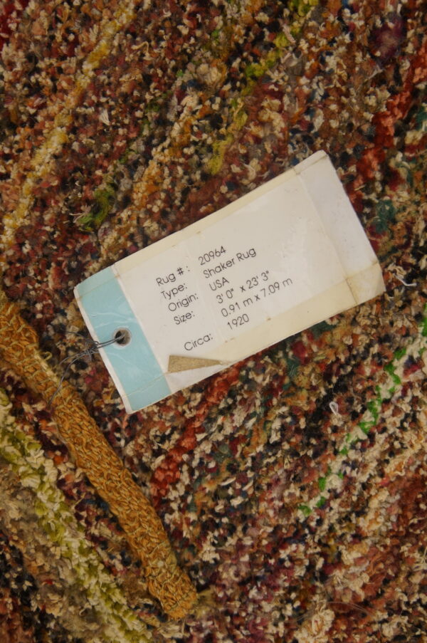 Close-up of variegated brown, red, and cream high-pile rug texture with a large white product information tag attached.