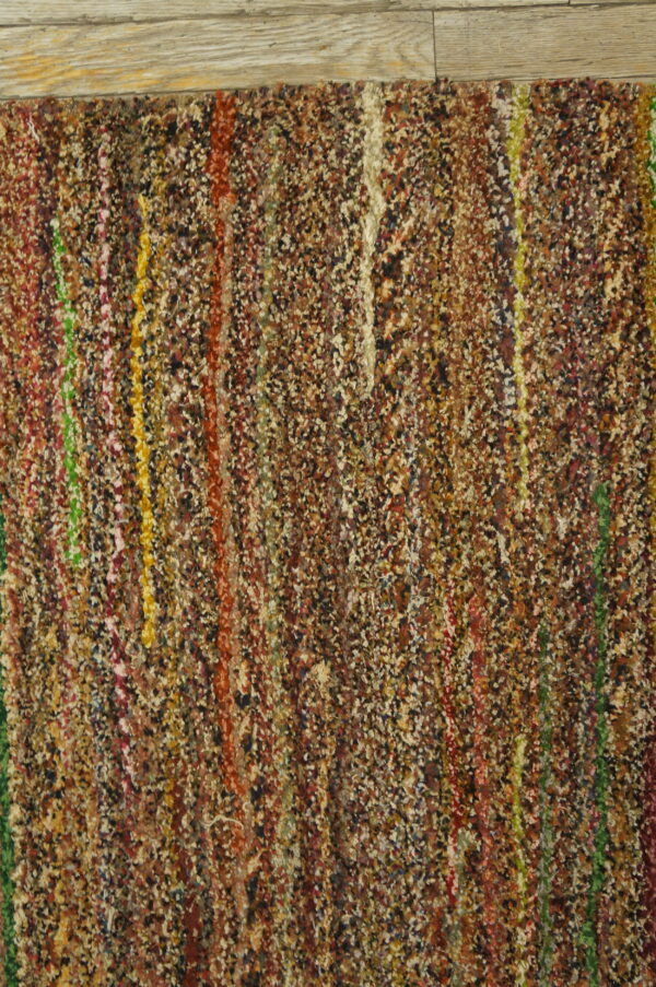 A multicolored, high-texture rug with speckled brown and bright vertical stripes next to light wood flooring.