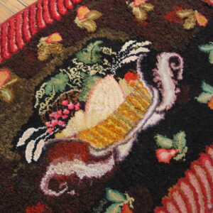 Textured, dark brown and black rug with a multicolored, central bird pattern and striped red border on wood floors.