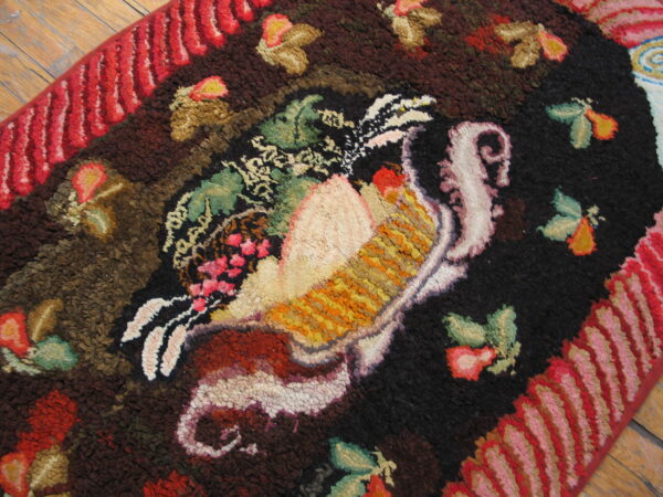 Textured, dark brown and black rug with a multicolored, central bird pattern and striped red border on wood floors.