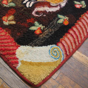 Textured corner of a multicolor rug with dark field, bright fruit patterns, and pink and red looped borders on wood planks.
