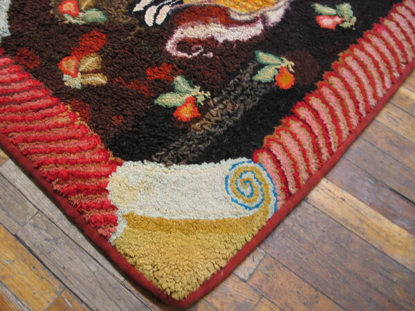 Textured corner of a multicolor rug with dark field, bright fruit patterns, and pink and red looped borders on wood planks.