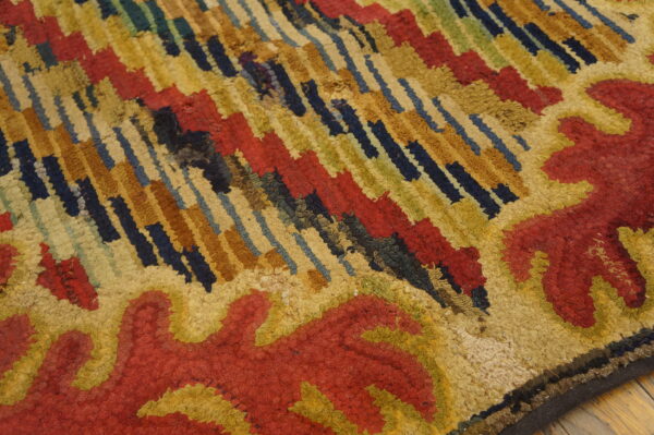 Textured rug close-up with thick red, gold, navy, and green abstract patterns over wood planks.