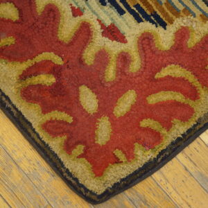 Textured corner of a red, yellow, and tan floral patterned rug resting on rustic wood plank flooring.