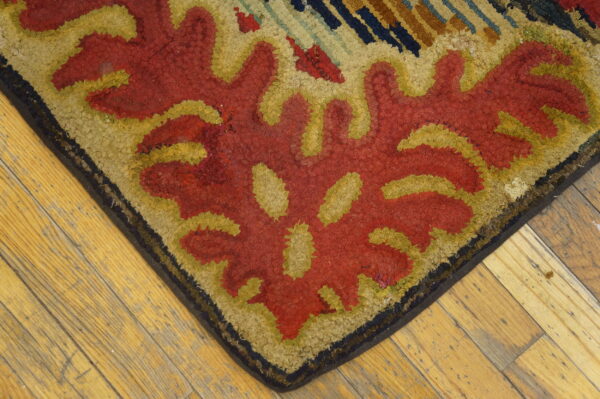 Textured corner of a red, yellow, and tan floral patterned rug resting on rustic wood plank flooring.
