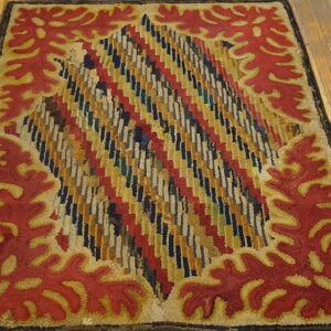 Rectangular rug with red stylized leaf border and a multicolored geometric central design on wood flooring.