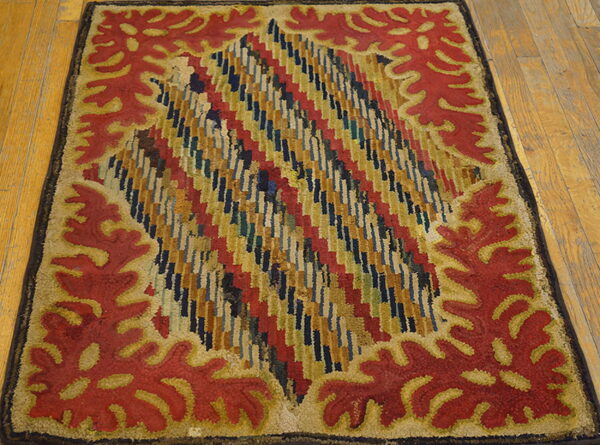 Rectangular rug with red stylized leaf border and a multicolored geometric central design on wood flooring.