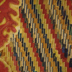 Close-up of a shaggy rug showing a red and gold scroll border next to a field of staggered multicolor stripes.