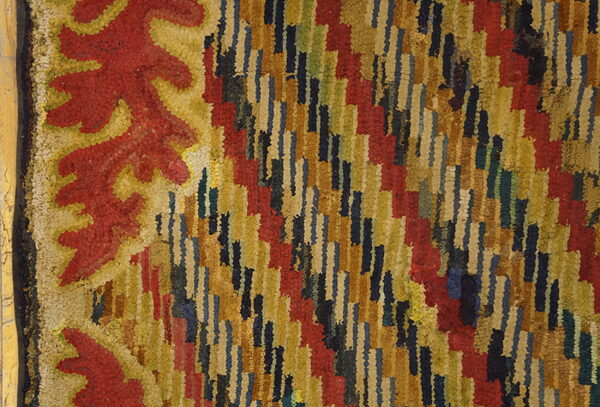 Close-up of a shaggy rug showing a red and gold scroll border next to a field of staggered multicolor stripes.