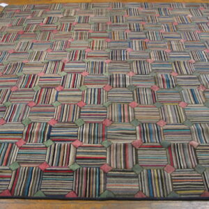 High-pile rug with a checkered pattern of multicolored striped blocks and pink and green accents on a wood floor.