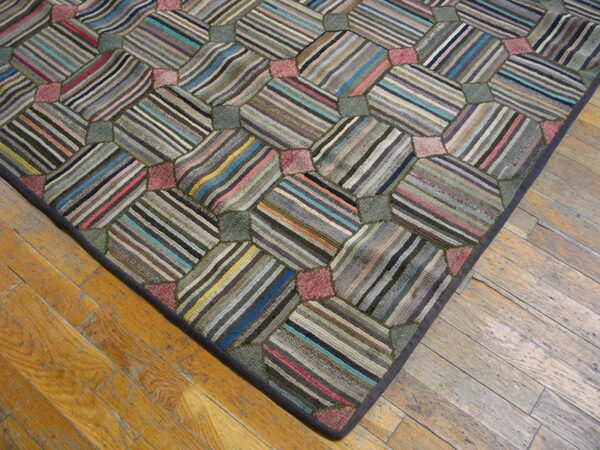 Low-pile rug with a tessellating pattern of striped patches in muted colors on worn wood floorboards.