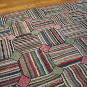 Multicolored patchwork rug with striped hexagonal shapes connected by pink and green diamonds on wood floor.