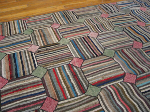 Multicolored patchwork rug with striped hexagonal shapes connected by pink and green diamonds on wood floor.