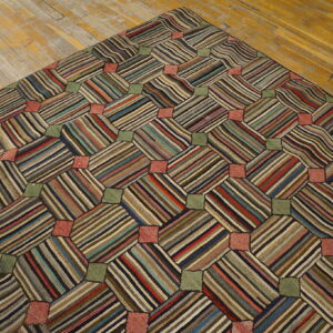 Patchwork rug with multicolored striped octagons and solid green and pink squares rests on distressed wood floor.