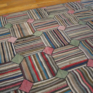 Geometric patchwork rug composed of multicolored striped panels connected by solid pink and sage green shapes on a wood floor.