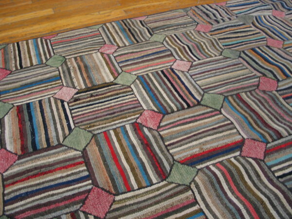 Geometric patchwork rug composed of multicolored striped panels connected by solid pink and sage green shapes on a wood floor.