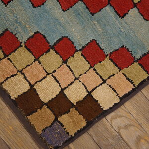 Textured rug corner featuring multicolored diamonds and a light blue field on distressed wood flooring.