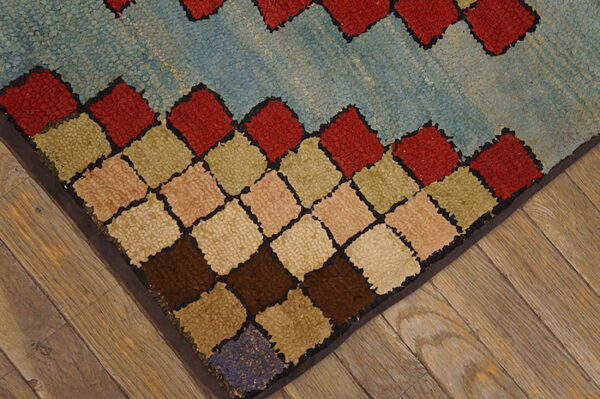 Textured rug corner featuring multicolored diamonds and a light blue field on distressed wood flooring.