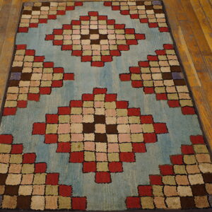 Low-pile rug with colorful red, brown, and green squares forming diamonds on a light blue ground over wood floorboards.