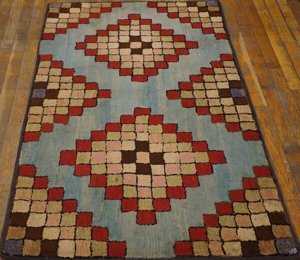 Low-pile rug with colorful red, brown, and green squares forming diamonds on a light blue ground over wood floorboards.