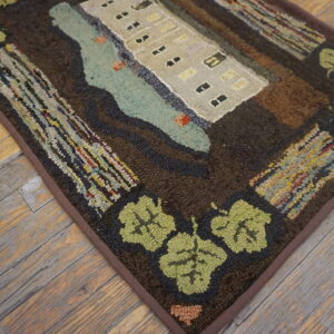 A pictorial hooked rug featuring a beige building, blue water, and green leaf border on distressed wood floors.