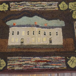 Primitive hooked rug featuring a central house and sky scene bordered by dark brown and green leaves on wooden flooring.