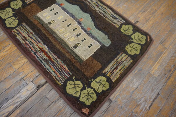 Hooked rug featuring a beige apartment building, blue water, and green leaves on rustic hardwood flooring.