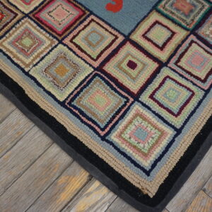 Highly textured rug with multicolored concentric diamonds and a black banded border on distressed wood plank flooring.