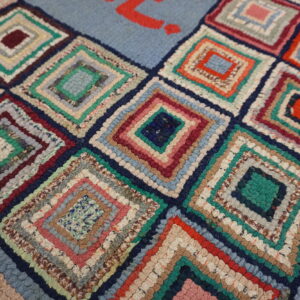High-texture rug featuring multicolored log cabin squares and a red design on a pale blue field.