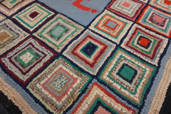 High-texture rug featuring multicolored log cabin squares and a red design on a pale blue field.