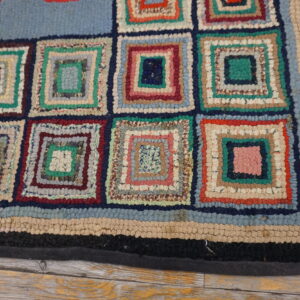 A multicolored rug with a looped texture and log cabin square pattern rests on light wood.