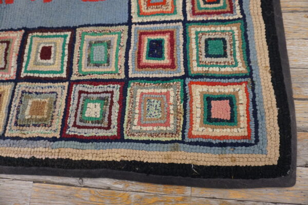 A multicolored rug with a looped texture and log cabin square pattern rests on light wood.