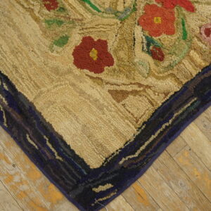 A chunky hooked rug featuring red and green floral designs on a beige field rests on distressed light wood planks.