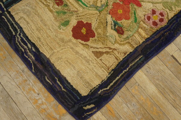 A chunky hooked rug featuring red and green floral designs on a beige field rests on distressed light wood planks.