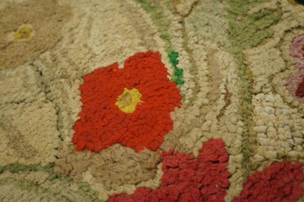 Textured floral rug close-up features red, yellow, and green elements on a chunky beige and tan pile.