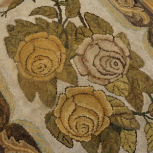 Textured rug featuring gold and pale pink roses, olive leaves, and brown borders on wood flooring.