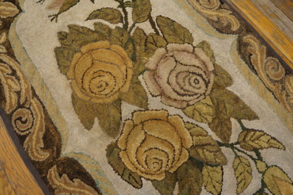 Textured rug featuring gold and pale pink roses, olive leaves, and brown borders on wood flooring.