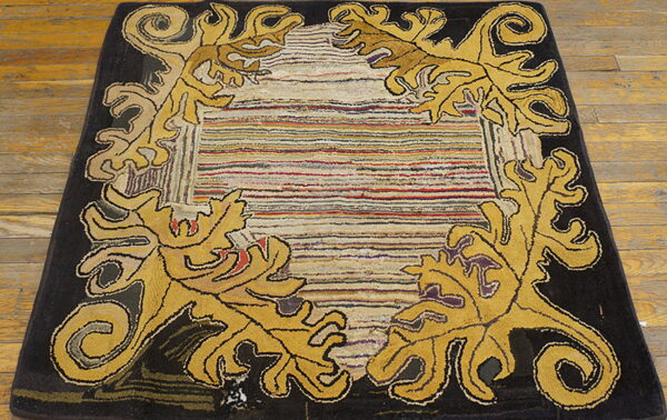 Black and gold rug featuring acanthus leaves and a multicolored striped center lies on wood flooring.