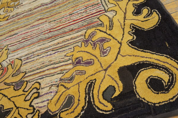Close-up of a rug showing yellow and black scrollwork bordering a striped textured field in multiple colors.