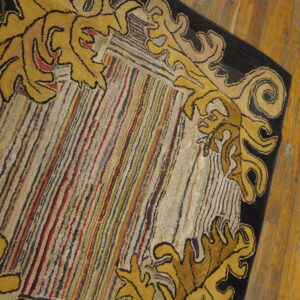 A textured rug with a black and yellow scrolling floral border surrounding a multicolored striped center on wood floors.