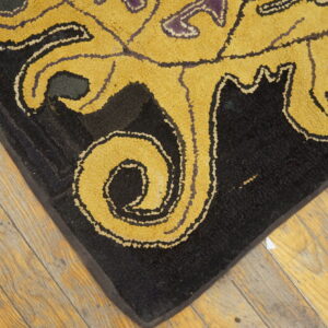 Textured black rug corner featuring bold, gold, scrolling patterns on light wood flooring.